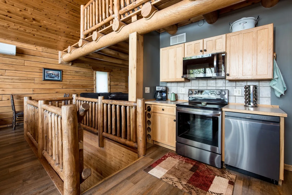 Kitchen angle showing cabinetry, countertops, and stainless steel appliances under log ceiling