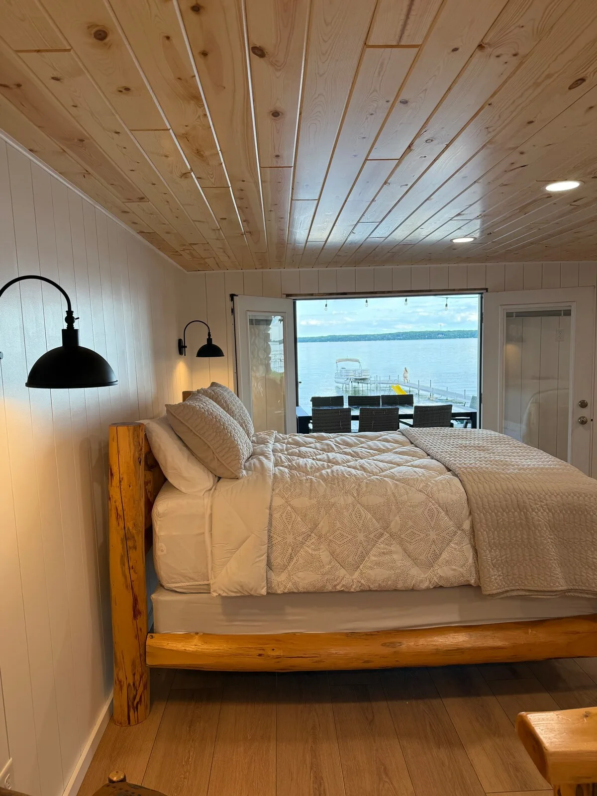 Sandbar Suite queen bed with lake view through window, log nightstand, and reading lamp