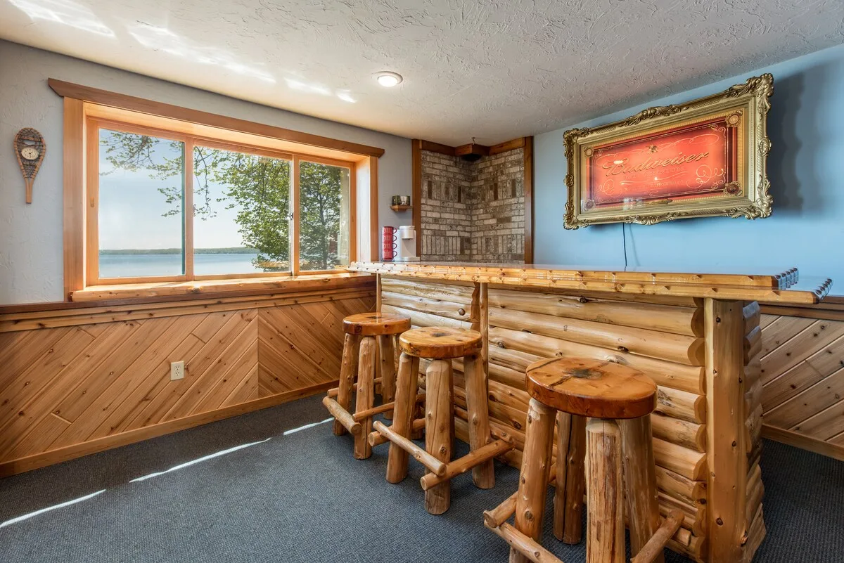 Lower level wet bar with log stools, stone accents, and recessed lighting