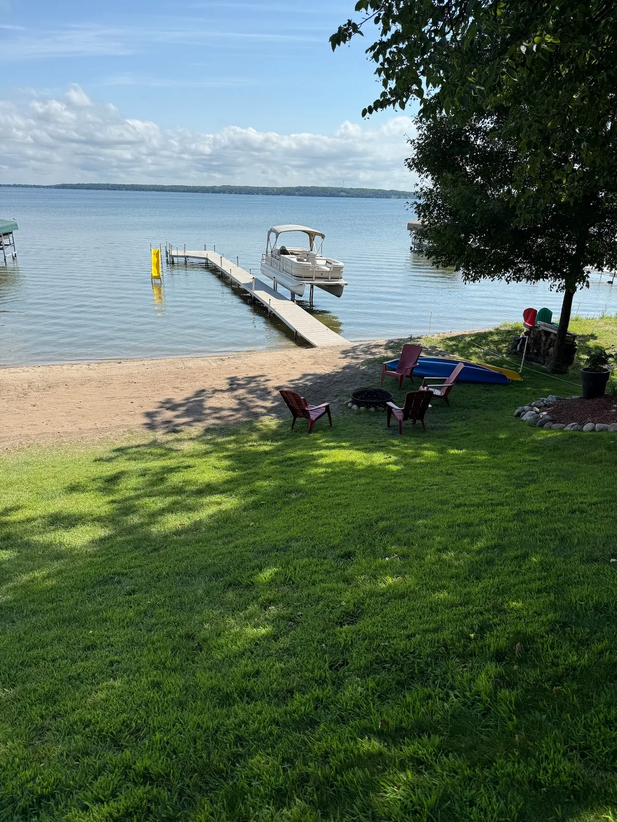 Private sandy beach with fire pit, dock, pontoon boat, and golden sunset light on the water