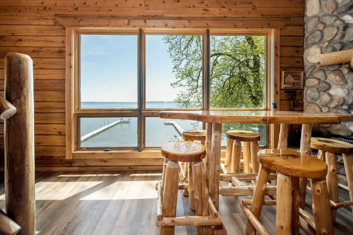 Log bar table with stools overlooking Lake Miltona through picture windows, stone fireplace alongside