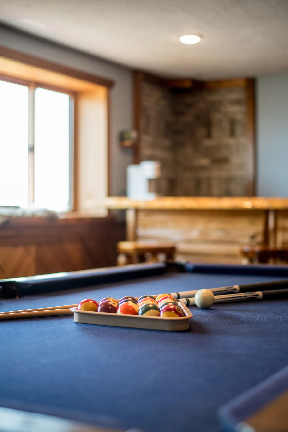 Pool table close-up with racked billiard balls and cues, bar visible in background