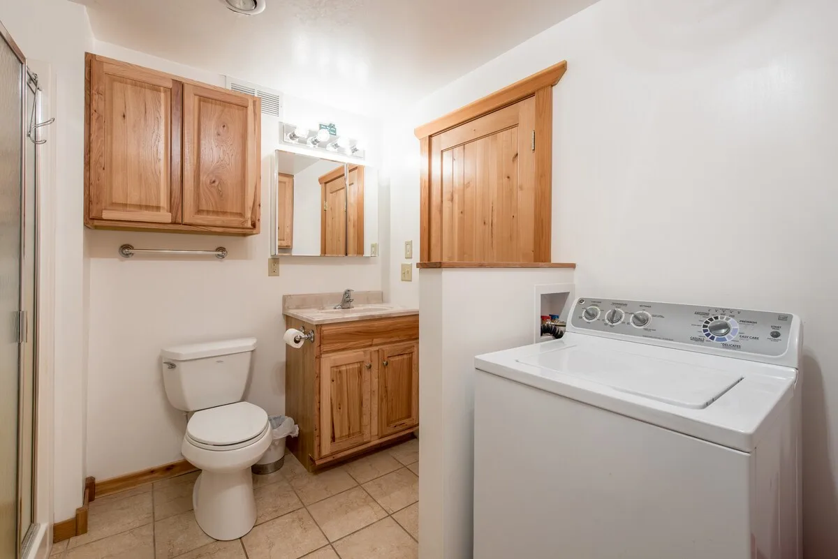 Lower level bathroom with shower stall, toilet, wooden cabinetry, and washing machine
