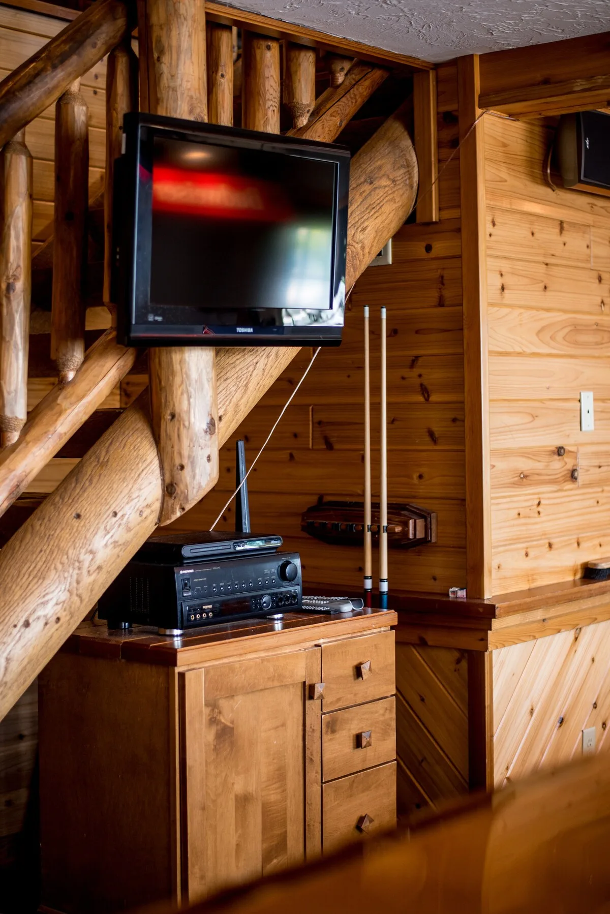 Game room TV and entertainment center with pool cues under the log staircase