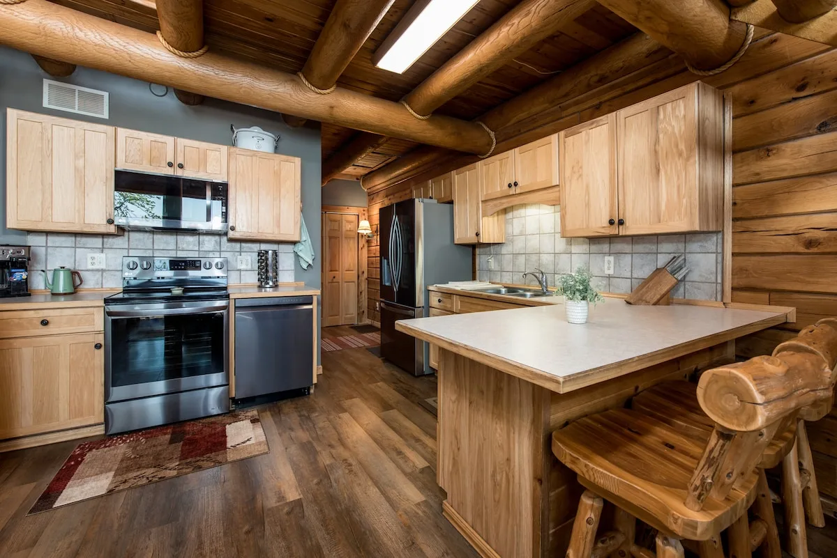 Fully equipped kitchen with stainless steel appliances, island with bar seating, and log beam ceiling with skylight