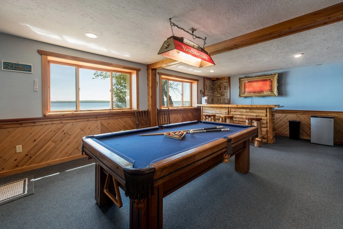 Lower level game room with pool table, Budweiser light, wet bar, and lake views through windows
