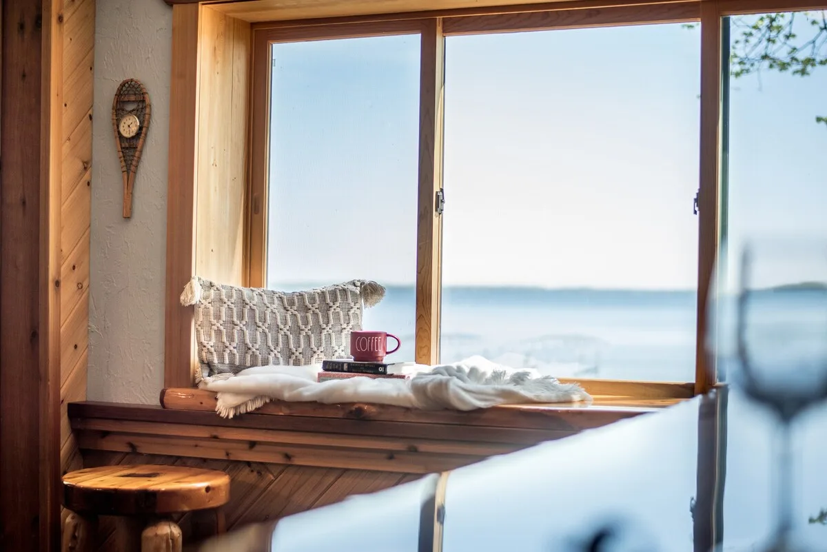 Window nook with pillow, coffee mug, books, and blanket overlooking the lake