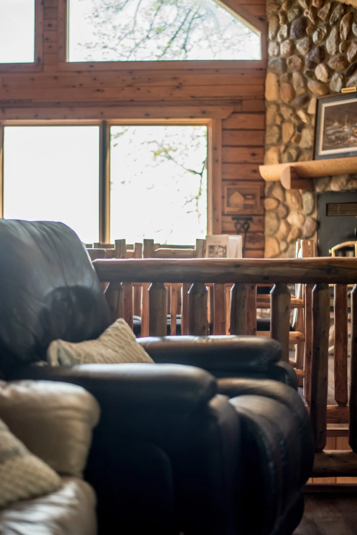 Leather recliner by the window with log railing and stone fireplace in background