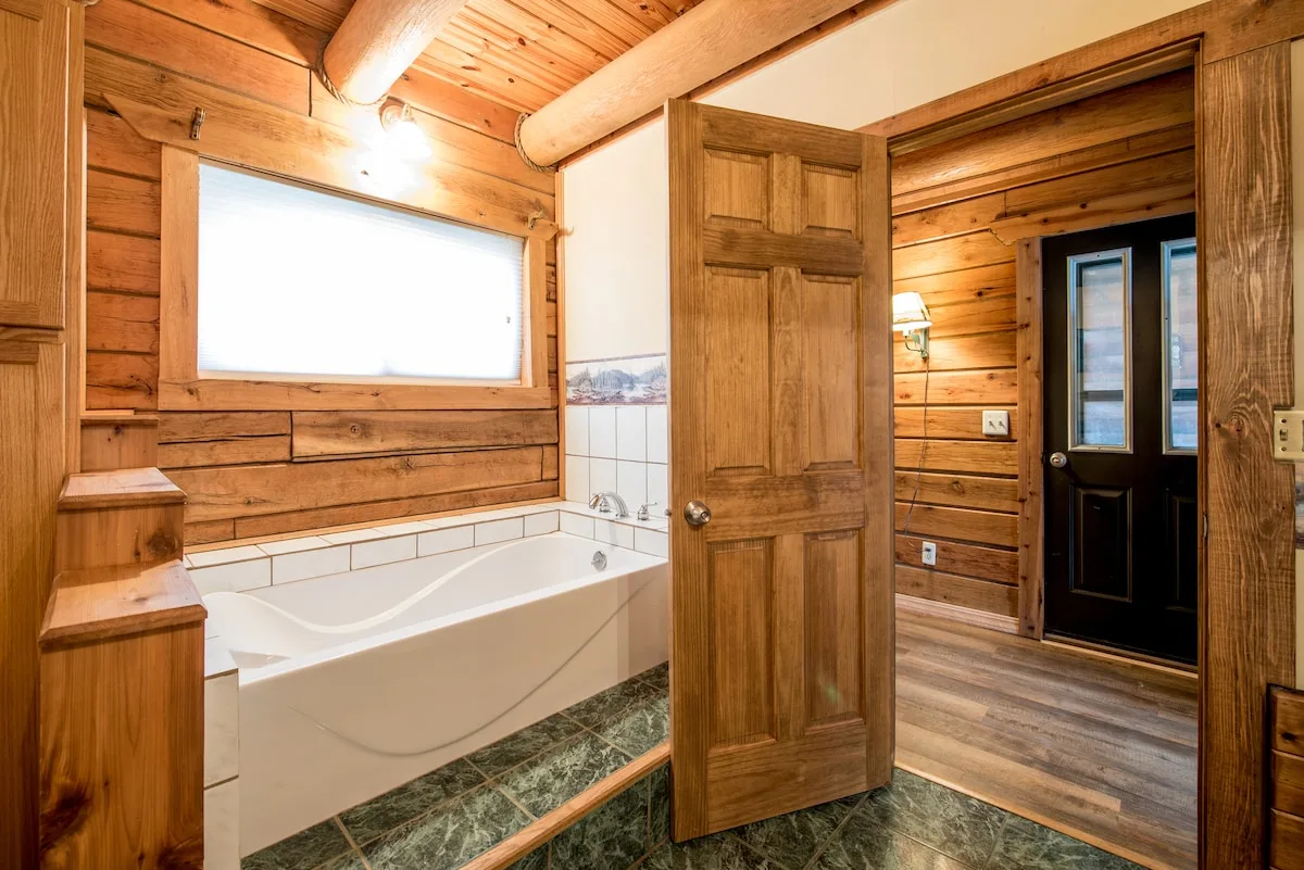 Master bathroom with soaking tub, log wall paneling, and frosted window