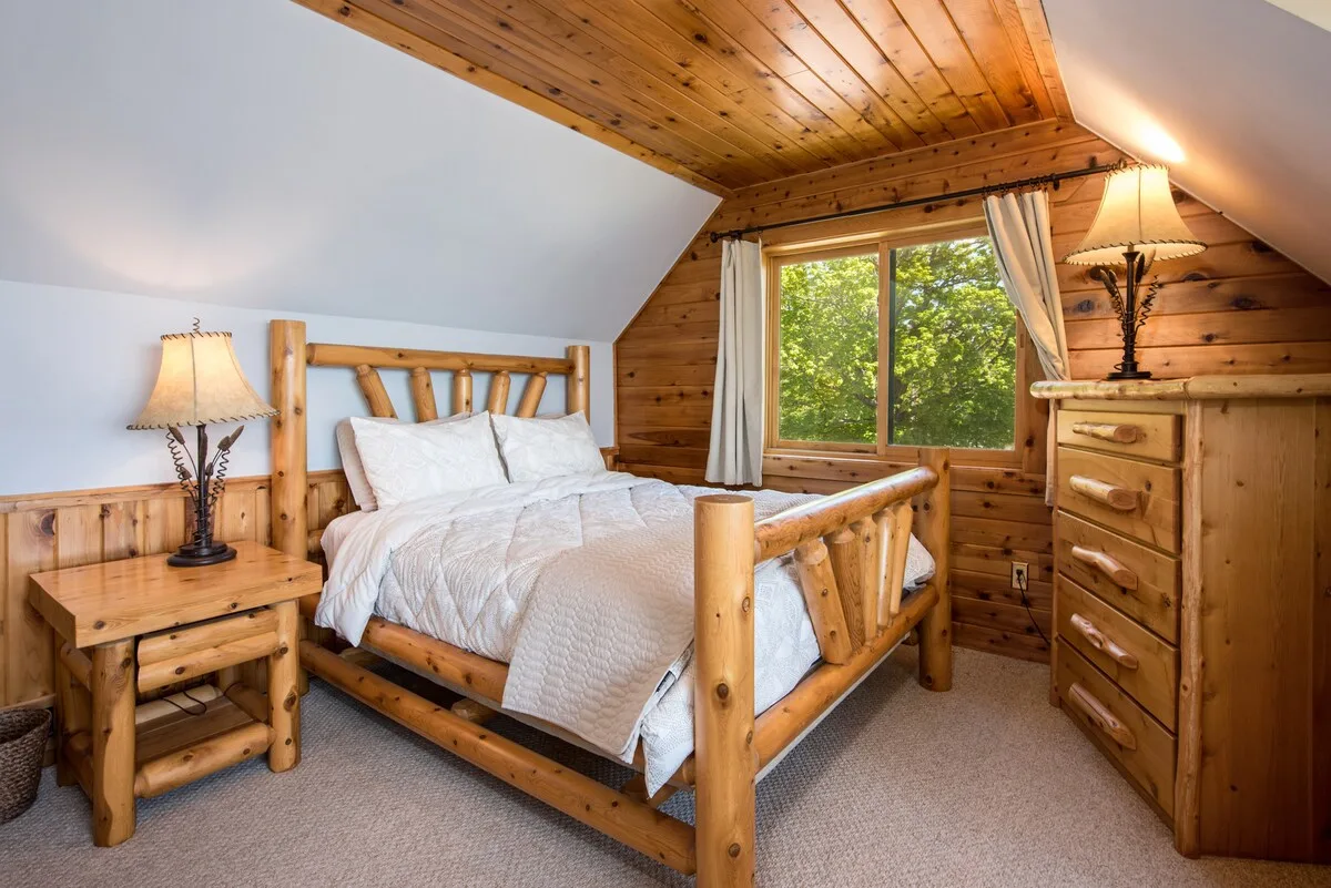Master bedroom queen bed with rustic log frame, vaulted wood ceiling, and warm lighting