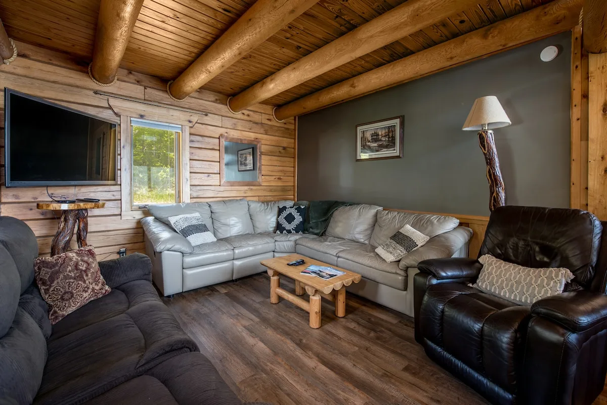 Living room with leather sectional sofa, recliner, flat-screen TV, and log beam ceiling