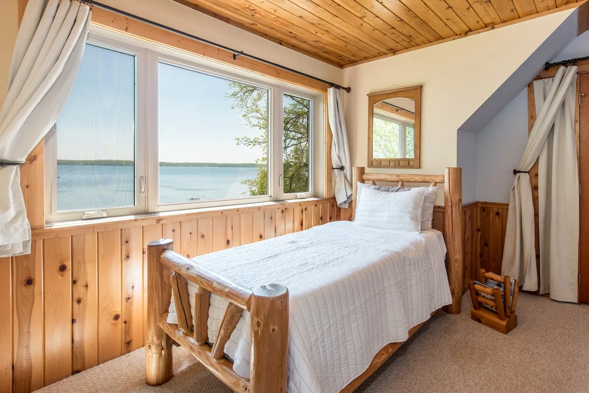 Sandbar Suite single bed with lake view through large windows and cedar wainscoting