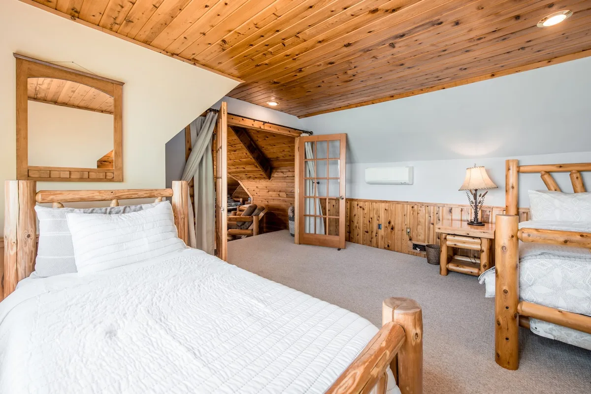 Loft bedroom with two log beds, french doors to sitting area, and vaulted cedar ceiling