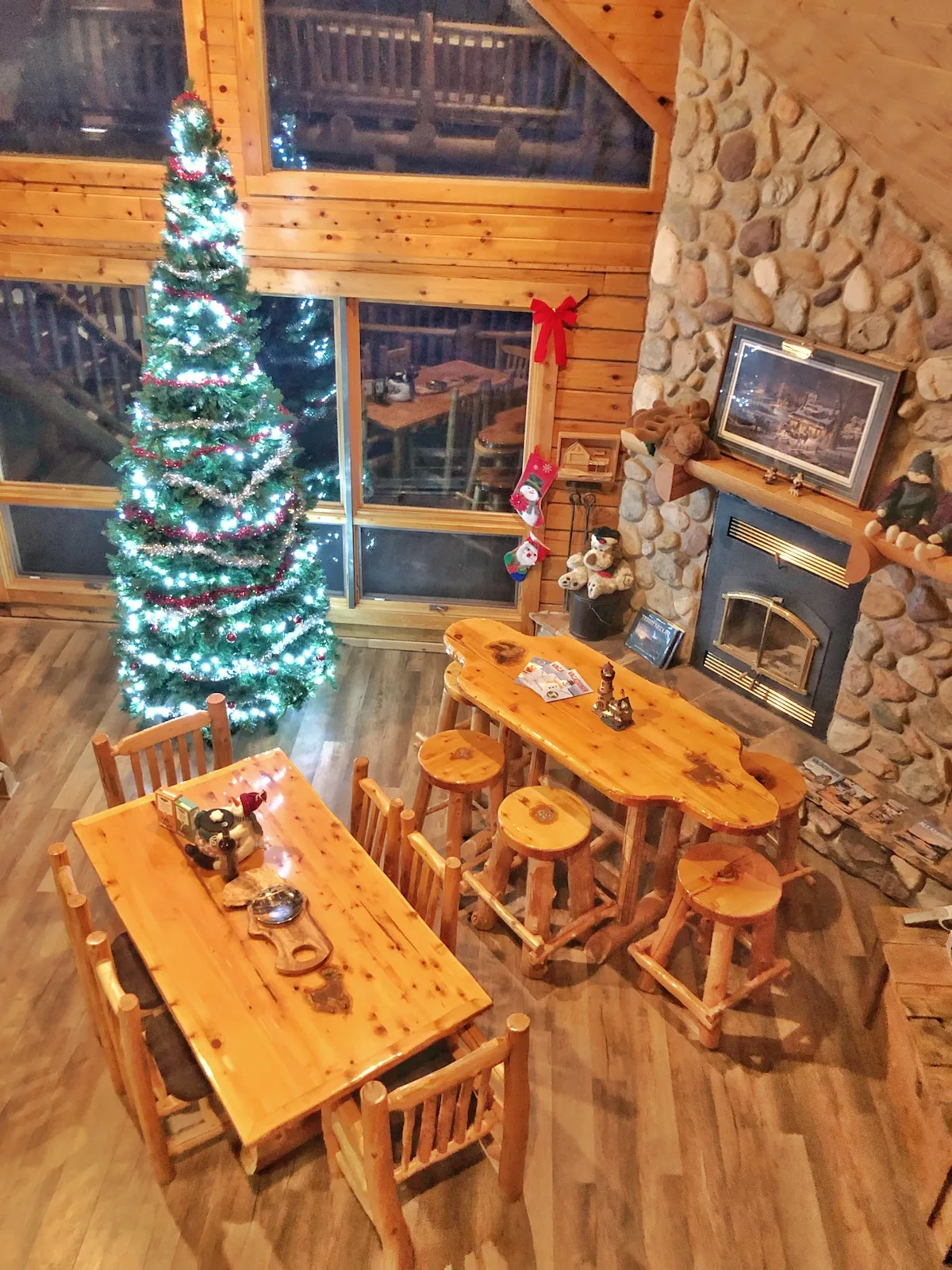 Great room decorated for the holidays with Christmas tree, log furniture, and stone fireplace from loft above