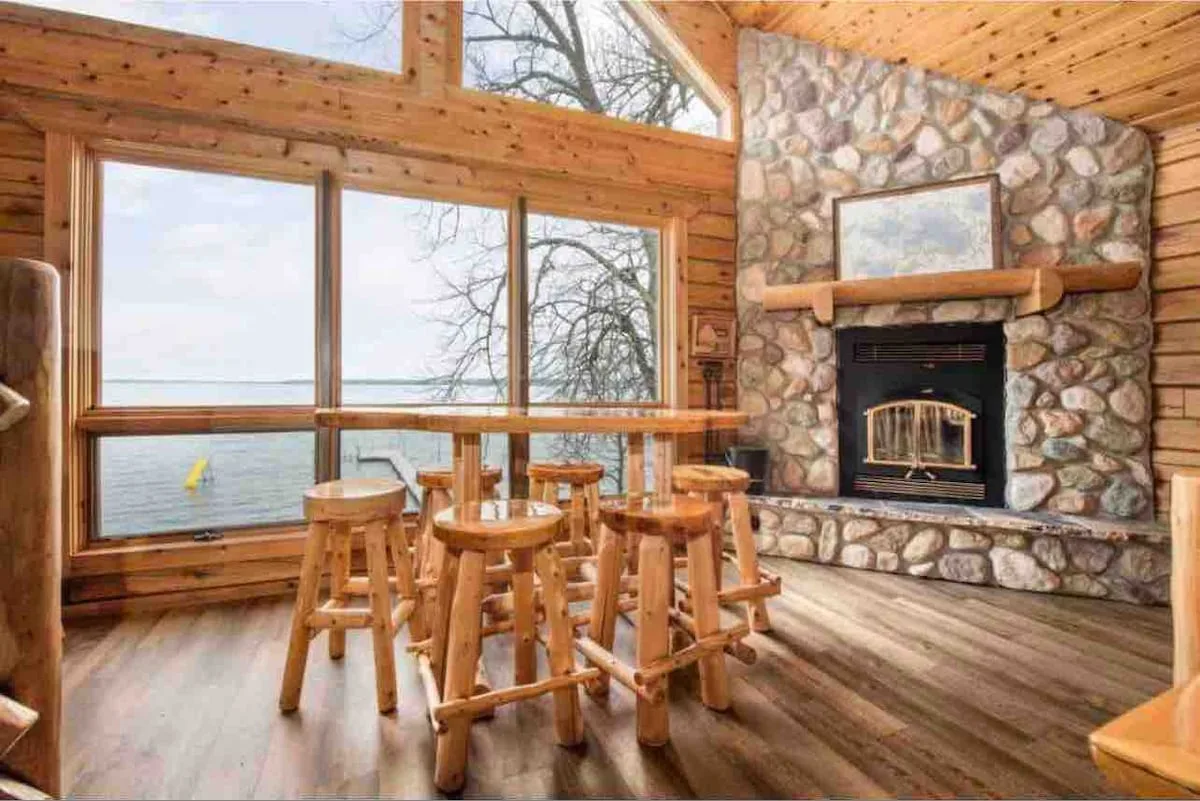 Stone fireplace with log mantel, bar-height seating, and floor-to-ceiling lake view windows