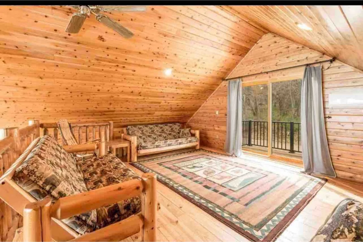 Loft sitting area with two futon sofas, rustic rug, sliding door to deck, and vaulted wood ceiling