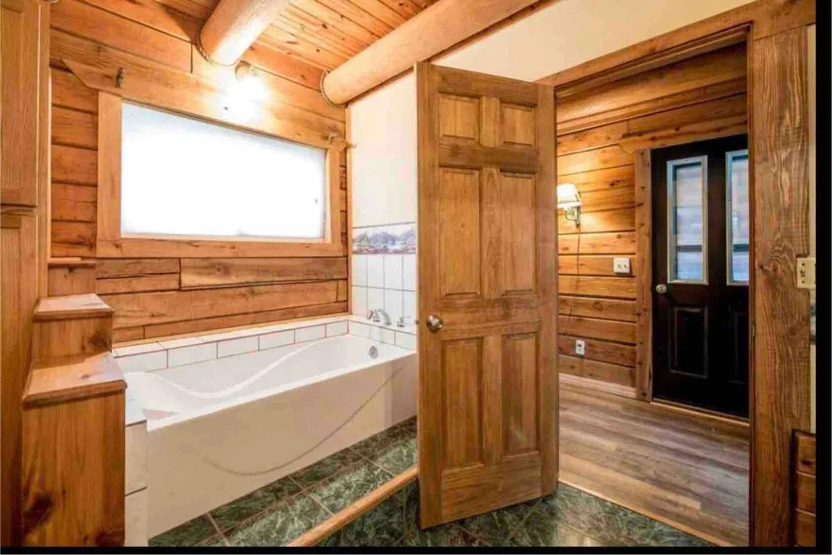Master bathroom soaking tub alternate angle with wood door and marble-tiled floor