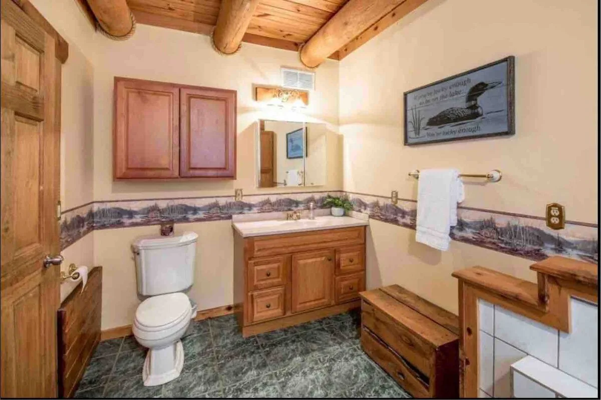 Main floor bathroom with loon painting, scenic wallpaper border, and log ceiling beams