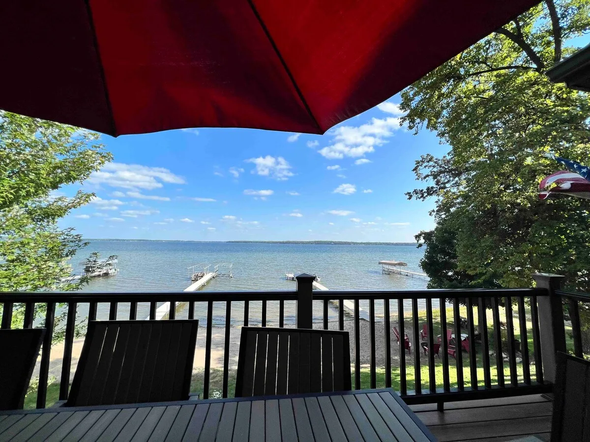 Upper deck dining area with lake views, red umbrella, dock, and beach visible below