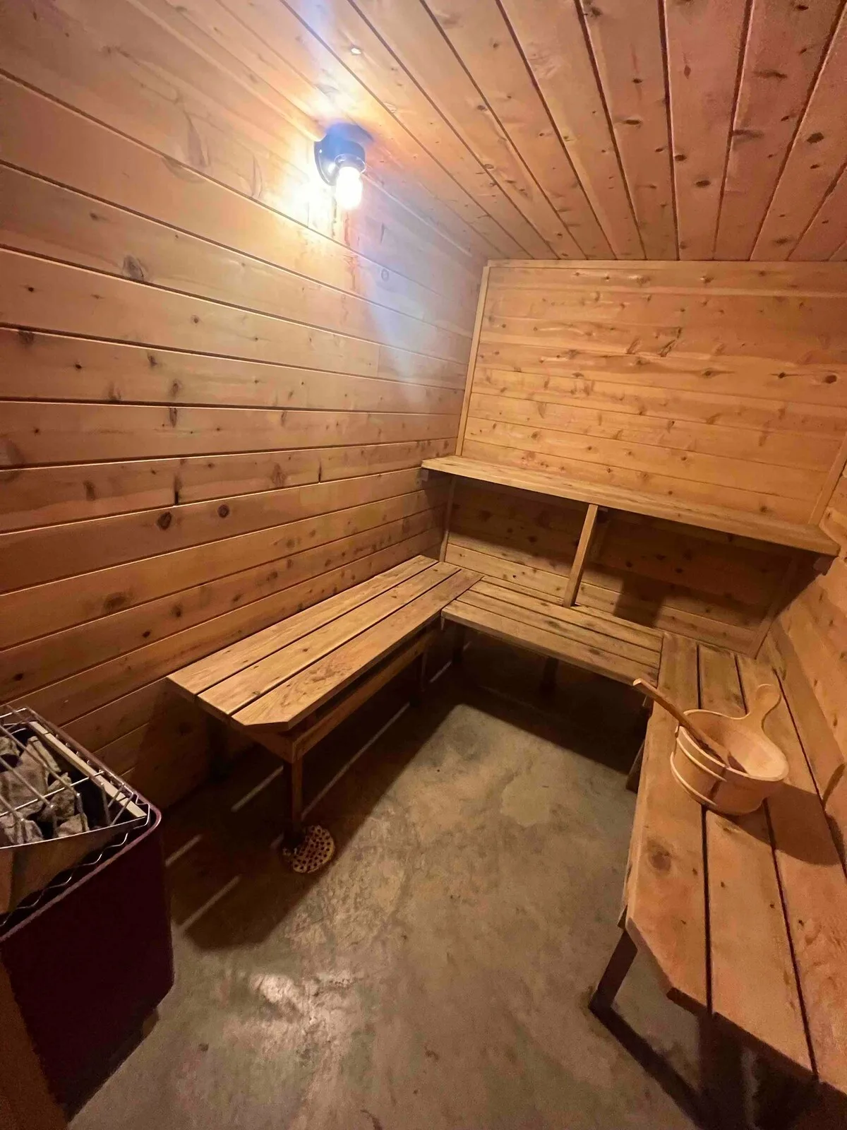 Private cedar sauna with bench seating, heater with rocks, and wooden bucket